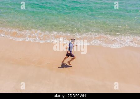 Coureur courant sur la plage au bord de l'océan - vue d'en haut. Homme athlète entraînement cardio jogging faire l'entraînement du matin. Vue de drone aérienne de héros, beaucoup Banque D'Images