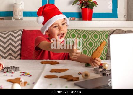 Vœux en ligne de Noël d'un garçon dans un chapeau de père Noël à l'aide d'une tablette. Bonne année Covid 2021. Banque D'Images