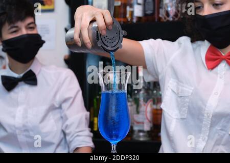 Serveuse non reconnaissable portant un masque de protection pour préparer des cocktails dans un pub. Nouvelle norme dans les pubs. Banque D'Images