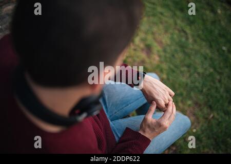 Homme avec une montre intelligente, mesurant la fréquence cardiaque. Cœur sur l'affichage intelligent de l'horloge. Concept de vie saine. Assis sur l'herbe. Banque D'Images