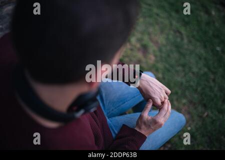 Homme avec une montre intelligente, mesurant la fréquence cardiaque. Cœur sur l'affichage intelligent de l'horloge. Concept de vie saine. Assis sur l'herbe. Banque D'Images