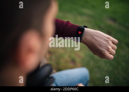 Homme avec une montre intelligente, mesurant la fréquence cardiaque. Cœur sur l'affichage intelligent de l'horloge. Concept de vie saine. Assis sur l'herbe. Banque D'Images