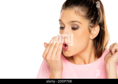 Jeune femme vérifiant sa respiration avec sa paume sur blanc arrière-plan Banque D'Images