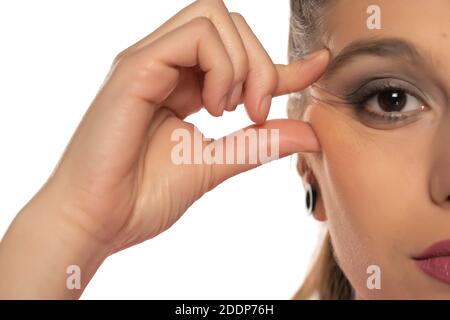 Une jeune femme se pinçant les rides de ses yeux sur fond blanc Banque D'Images