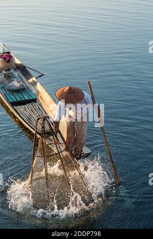 Intha leg rameur pêcheurs à Inle Lake, Myanmar (Birmanie), Asie en février - pêcheur abaissant le filet dans l'eau créant des éclaboussures Banque D'Images