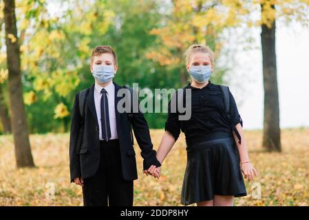 Des écoliers, des garçons et des filles sous des masques médicaux marchent dans le parc de la ville. Banque D'Images