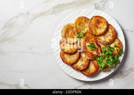 Crêpes de pommes de terre au fromage cottage à l'ail, persil, servies avec une sauce à la crème sure sur une assiette sur fond de pierre en marbre clair avec couverts dorés Banque D'Images