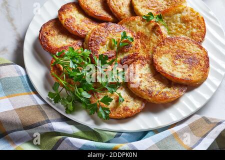 Crêpes de pommes de terre au fromage cottage à l'ail, persil, servies avec une sauce à la crème sure sur une assiette sur fond de pierre en marbre clair avec couverts dorés Banque D'Images