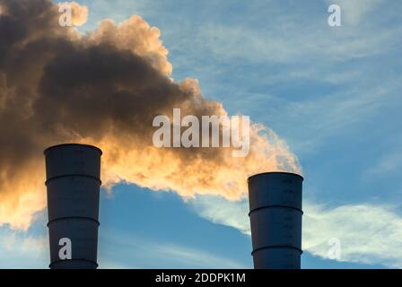 Cheminées industrielles qui déversons de la fumée et de la suie dans le ciel bleu polluer l'air et provoquer le réchauffement de la planète et le changement climatique avec les gaz à effet de serre et Banque D'Images