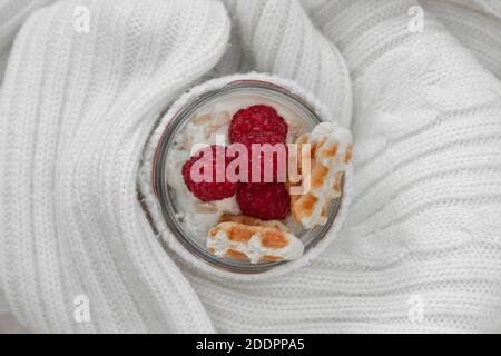 Fromage cottage avec framboises, muesli et gaufres, sur le yaourt dans un pot enveloppé dans un chandail blanc chaud. Banque D'Images