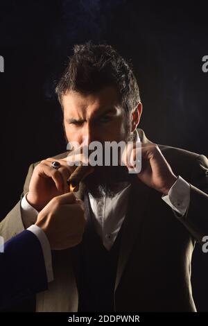 Homme avec barbe tient le cigare sur fond noir. Lampes de main mâles occupé businessmans cigare à fumer. Guy en costume classique a cinq minutes de pause pour fumer. Concept d'affaires et de mauvaise habitude. Banque D'Images