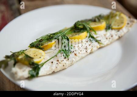 Un filet d'une ligne de bar pêché, Dicentrarchus labrax, qui a été cuit en papier, en papillote, avec des citrons, du beurre et du persil. Assaisonné de bl Banque D'Images