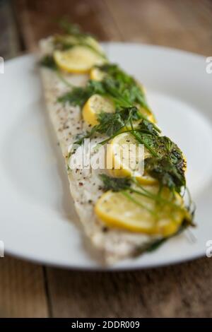 Un filet d'une ligne de bar pêché, Dicentrarchus labrax, qui a été cuit en papier, en papillote, avec des citrons, du beurre et du persil. Assaisonné de bl Banque D'Images