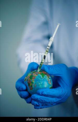 gros plan d'un médecin, sous un manteau blanc et des gants chirurgicaux bleus, vaccinant un globe terrestre Banque D'Images