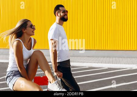 Un gars et une fille ont plaisir à monter sur un chariot près du supermarché, un couple aimant posant assis sur un chariot, un été Sunny jour Banque D'Images