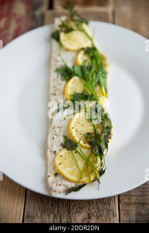 Un filet d'une ligne de bar pêché, Dicentrarchus labrax, qui a été cuit en papier, en papillote, avec des citrons, du beurre et du persil. Assaisonné de bl Banque D'Images