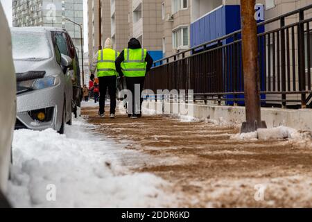 Deux ouvriers en gilets réfléchissants jaunes saupoudrer de sable sur une passerelle à partir d'un chariot. Banque D'Images