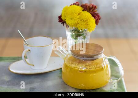 Thé d'argousier sain dans une théière en verre à côté de la tasse et vase de fleurs Banque D'Images