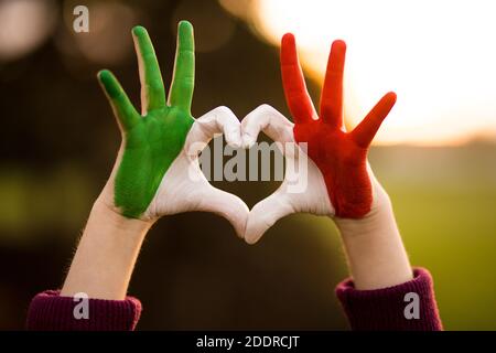 Forme de coeur des enfants peint à la main dans les couleurs de drapeau d'italie, langue du corps des enfants, concept d'amour des enfants. Cœur main sur la nature coucher de soleil arrière-plan bokeh Banque D'Images