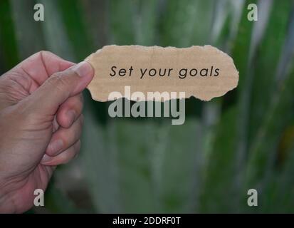 Mains tenant du papier déchiré avec citation motivationnelle et arrière-plan vert flou. Citation inspirante Banque D'Images