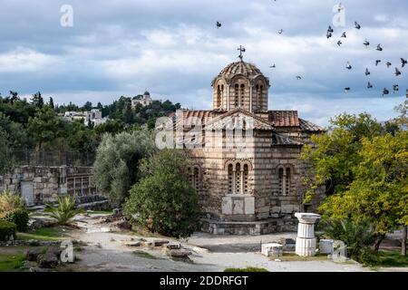 Troupeau de pigeons volant autour de l'église orthodoxe grecque dans la région de Thissio, Athènes, Grèce. Bâtiment de l'observatoire national et ciel nuageux. Banque D'Images