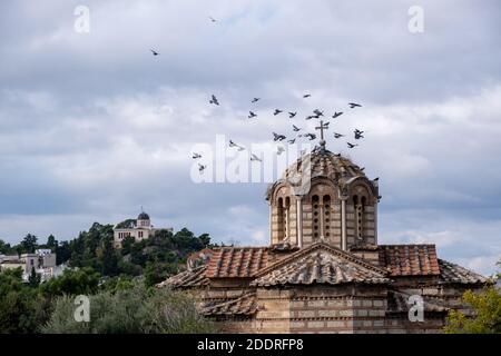 Troupeau de pigeons volant autour du dôme de l'église orthodoxe grecque dans la région de Thissio, Athènes, Grèce. Bâtiment de l'observatoire national et ciel nuageux backgro Banque D'Images