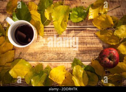 Vue du haut composition automnale avec des feuilles jaunes et vertes sur fond de bois brûlé avec une tasse de thé et de pomme. Avec espace libre pour le texte Banque D'Images