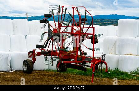 Machine agricole à rotor rouge avec ensilage de balle de foin de graminées enveloppé en plastique blanc à l'arrière-plan. . Photo de haute qualité Banque D'Images