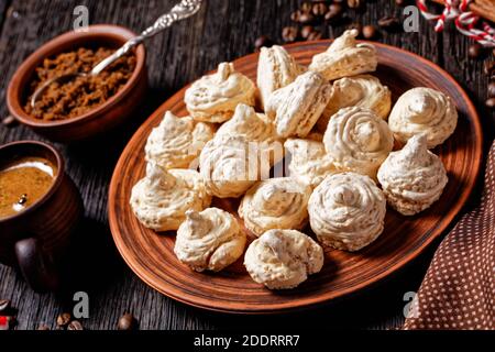 Biscuits meringue servis sur une assiette avec canne à sucre de noël, tasses à café, grains de café, sucre brun et bâtons de cannelle sur fond de bois foncé, Banque D'Images