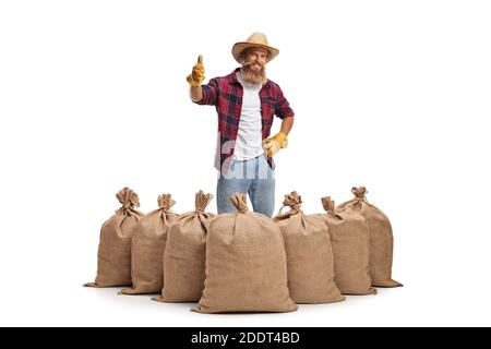 Joyeux fermier barbu debout derrière des sacs de burlap et montrant des pouces isolé sur fond blanc Banque D'Images