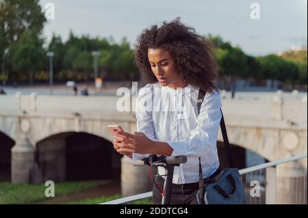 Une jeune femme télécharge l'application pour utiliser le scooter électrique en ville rue saine style de vie durable style de vie Banque D'Images