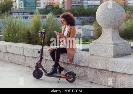 Une jeune femme télécharge l'application pour utiliser le scooter électrique en ville rue saine style de vie durable style de vie Banque D'Images