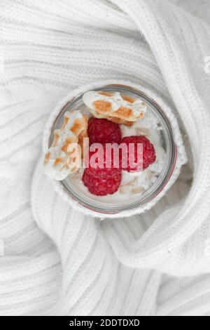 Fromage cottage avec framboises, muesli et gaufres, sur le yaourt dans un pot enveloppé dans un chandail blanc chaud. Banque D'Images