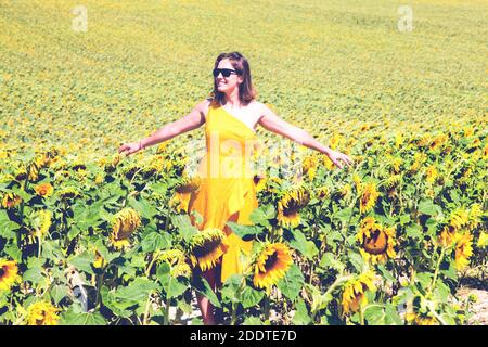 Jeune femme en robe jaune marchant dans le champ de tournesol en fleur. Concept de style de vie Banque D'Images