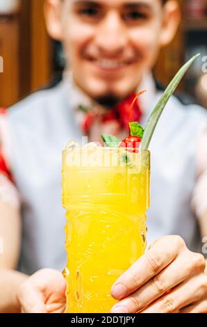 Barman montrant un cocktail dans un verre de tiki sur un bar compteur sur un fond flou de bouteilles dans une barre Banque D'Images