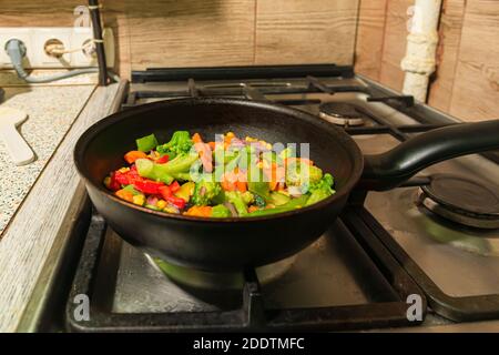 De nombreux légumes végétariens colorés sont frits dans une poêle sur la cuisinière. Pois, pisums, oignons, poivrons, poivrons, poivrons, brocolis, cor Banque D'Images