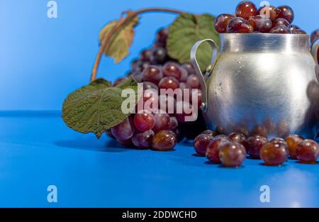 Fruits de raisin. Ingrédient pour les jus et le vin. Baies de raisin dans un récipient en aluminium. Arrière-plan bleu. Nourriture humaine Banque D'Images