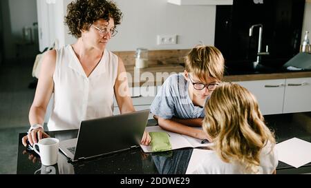 Photo de la jeune mère utilisant son ordinateur portable avec ses deux enfants adorables à la maison. Banque D'Images