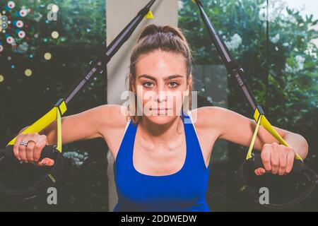 Belle fille de formation de ses bras avec des lanières TRx Fitness in La salle de gym - femme faisant des pompes entraîne le haut du corps épaules poitrine triceps pectoraux Banque D'Images