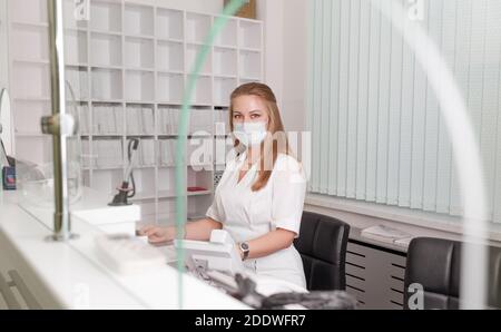 Fille-administrateur dans un manteau blanc et masque d'un médical Clinique.réception des patients.admission à l'hôpital Banque D'Images