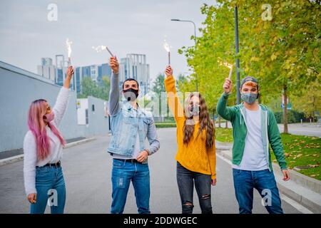 Groupe d'amis multiethniques qui se jocent avec des sparkers et portent le visage masques de sécurité tout en gardant la distance sociale pendant le coronavirus - Covid-19 spr Banque D'Images