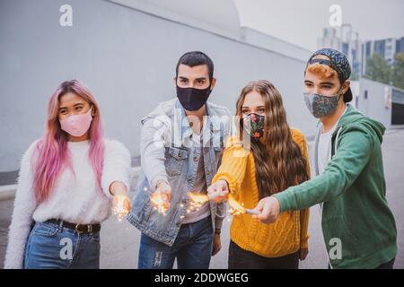 Groupe d'amis multiethniques qui se jocent avec des sparkers et portent le visage masques de sécurité tout en gardant la distance sociale pendant le coronavirus - Covid-19 spr Banque D'Images
