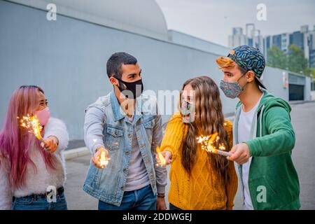Groupe d'amis multiethniques qui se jocent avec des sparkers et portent le visage masques de sécurité tout en gardant la distance sociale pendant le coronavirus - Covid-19 spr Banque D'Images