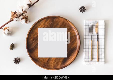 Carte de vœux en papier vierge sur plat en bois, couverts avec serviette à carreaux, fleurs en coton. Arrière-plan de table blanc. Flat lay, vue de dessus Banque D'Images