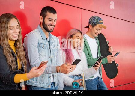 Un groupe de jeunes amis se latent de leur téléphone portable pendant debout contre un mur dans la ville - Teneegers utilisant téléphones mobiles intelligents Banque D'Images