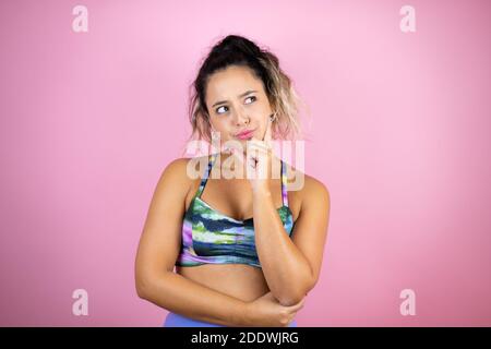 Jeune belle femme portant des vêtements de sport sur fond de réflexion rose isolé et en regardant sur le côté Banque D'Images