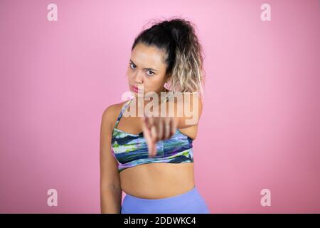 Jeune belle femme portant des vêtements de sport sur un arrière-plan rose isolé pointant vers l'avant avec le doigt Banque D'Images