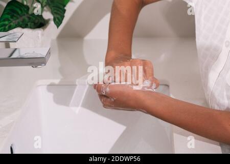 Photo de la personne non reconnue utilisant du savon et de l'eau pour nettoyer ses mains dans la salle de bains. Banque D'Images