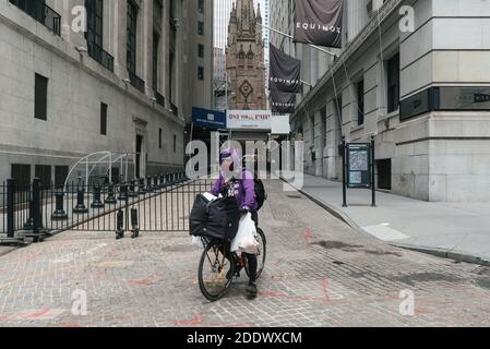 22 mai 2020. Manhattan, New York, États-Unis. Un liveur portant un masque facial sur un vélo sur un Wall Street vide à côté de la Bourse de New York. Banque D'Images