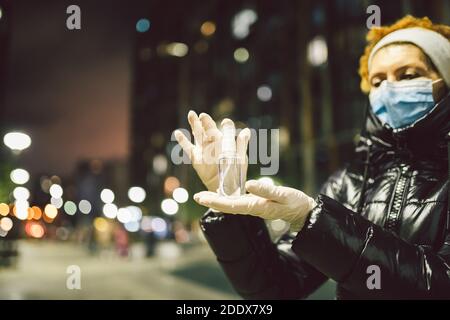 Protection coronavirus et covid 19. Antiseptique contre l'infection dans les mains de la femme mature dans la rue en soirée ville en hiver. Femme âgée en masque Banque D'Images